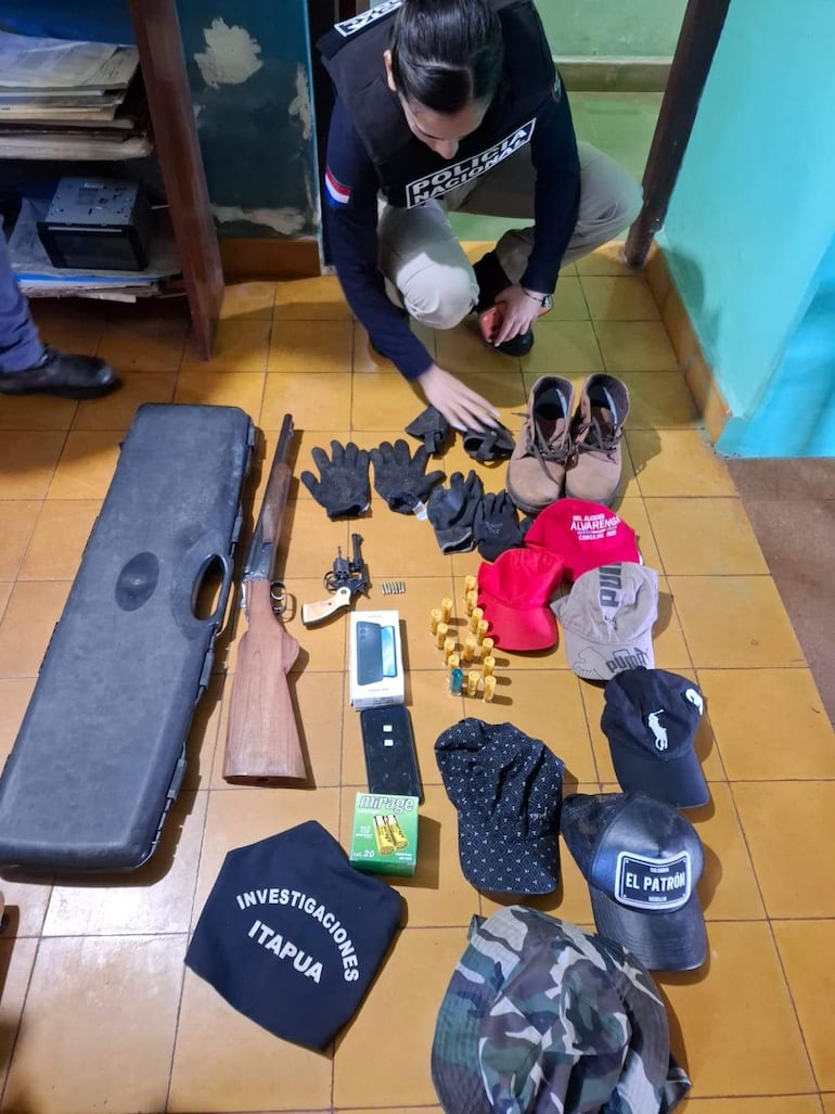 Mujer policía agachada organiza armas y objetos en el suelo, en un entorno desordenado de una operación policial.
