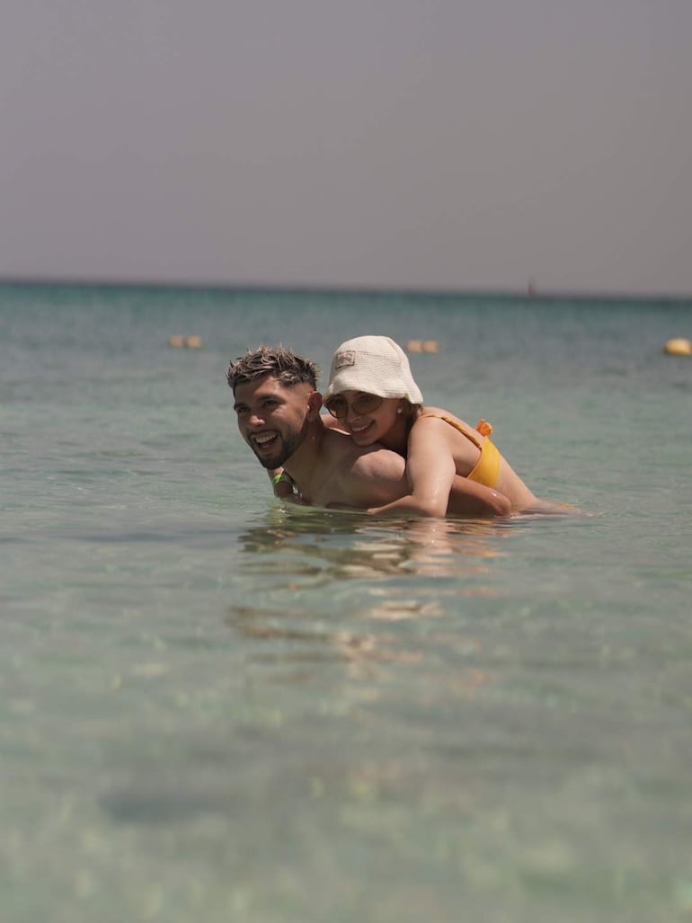 Julio Enciso sonríe en el agua con Ramón Sosa, quien lo abraza desde atrás, ambos luciendo relajados y felices.