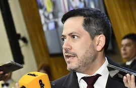 Raúl Latorre con traje oscuro y corbata, rodeado de micrófonos, hablando a periodistas en un entorno formal.