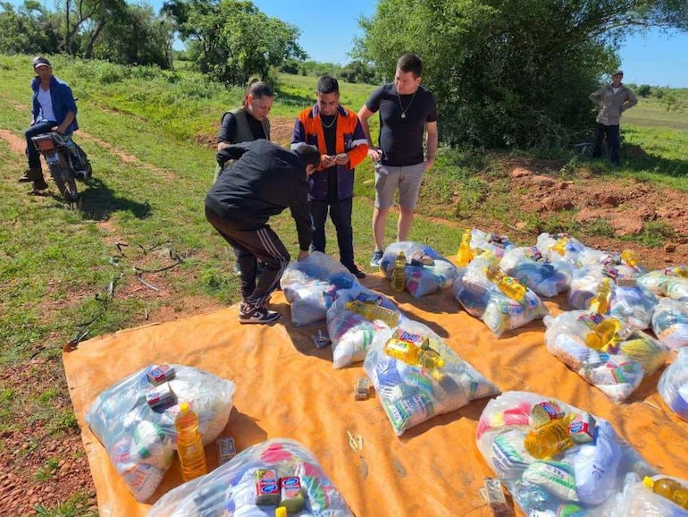Grupo de cinco hombres en entorno rural, revisando paquetes de alimentos sobre una lona anaranjada.