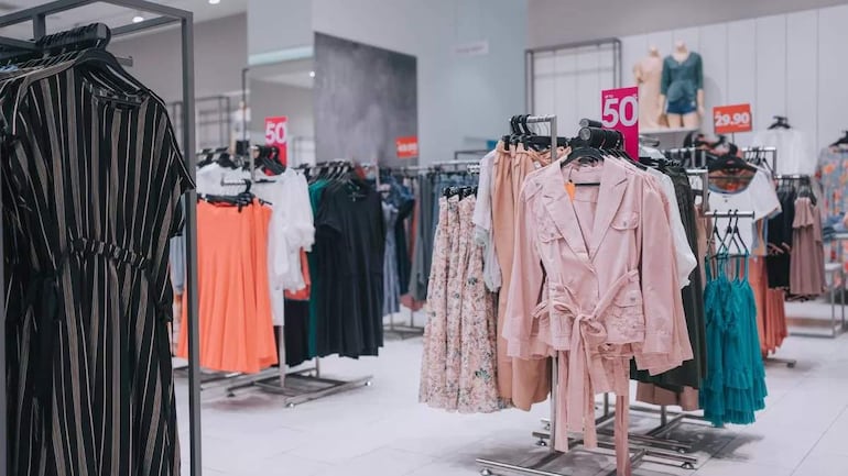 Tienda de ropa con racks organizados de vestidos y chaquetas en colores variados, resaltando etiquetas de precios.