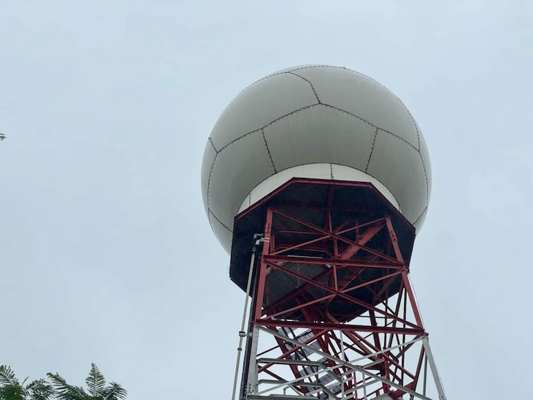 Soporte metálico rojo y blanco sostiene gran esfera blanca en campus de la UNA, cielo nublado al fondo.