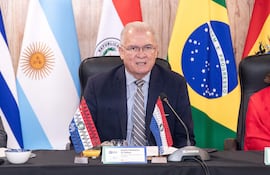 Dr. Emiliano Rolón Fernández habla en un panel, con traje oscuro y gafas, junto a banderas y una mujer escuchando atentamente.