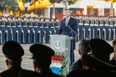 Santiago Peña en podio con expresión tranquila durante la ceremonia, rodeado de oficiales en uniforme y un arreglo floral.