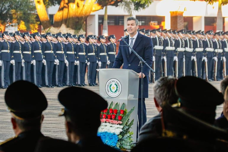 Santiago Peña en podio con expresión tranquila durante la ceremonia, rodeado de oficiales en uniforme y un arreglo floral.