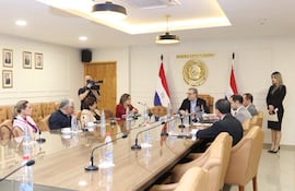 Rafael Augusto Filizzola Serra con gafas y chaqueta abierta, rodeado de seis personas sentadas en una mesa, en ambiente formal.