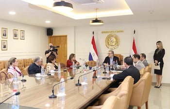 Rafael Augusto Filizzola Serra con gafas y chaqueta abierta, rodeado de seis personas sentadas en una mesa, en ambiente formal.