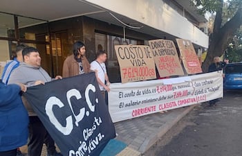 Grupo de activistas sosteniendo carteles y un gran banner negro en una manifestación urbana, con expresiones determinadas.