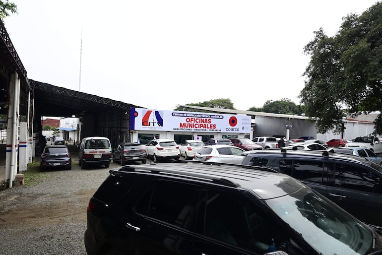 Estacionamiento con autos blancos y oscuros, cartel del Centro de Inspección Técnica Vehicular COARCO al fondo, clima nublado.