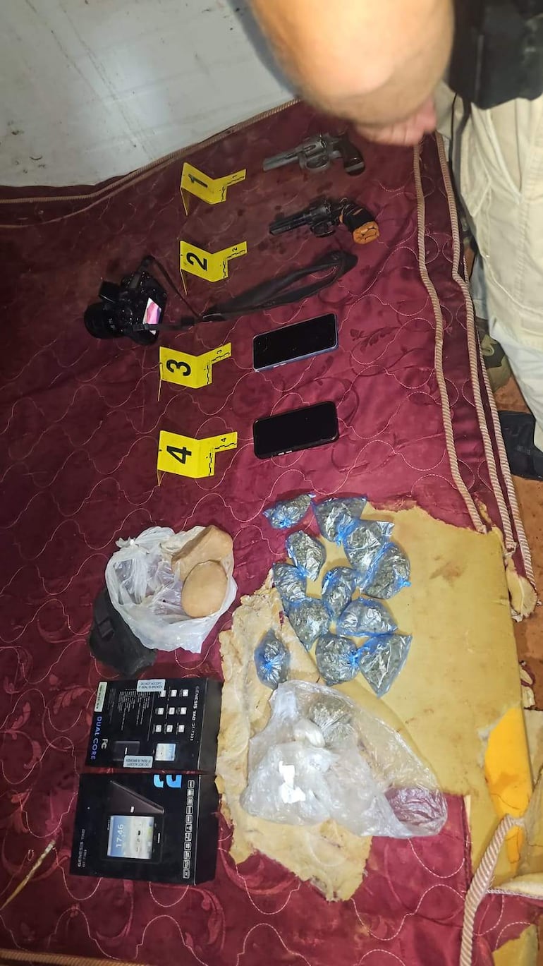 Tres hombres esposados y boca abajo en el suelo, rodeados de armas y teléfonos, en un ambiente policial.