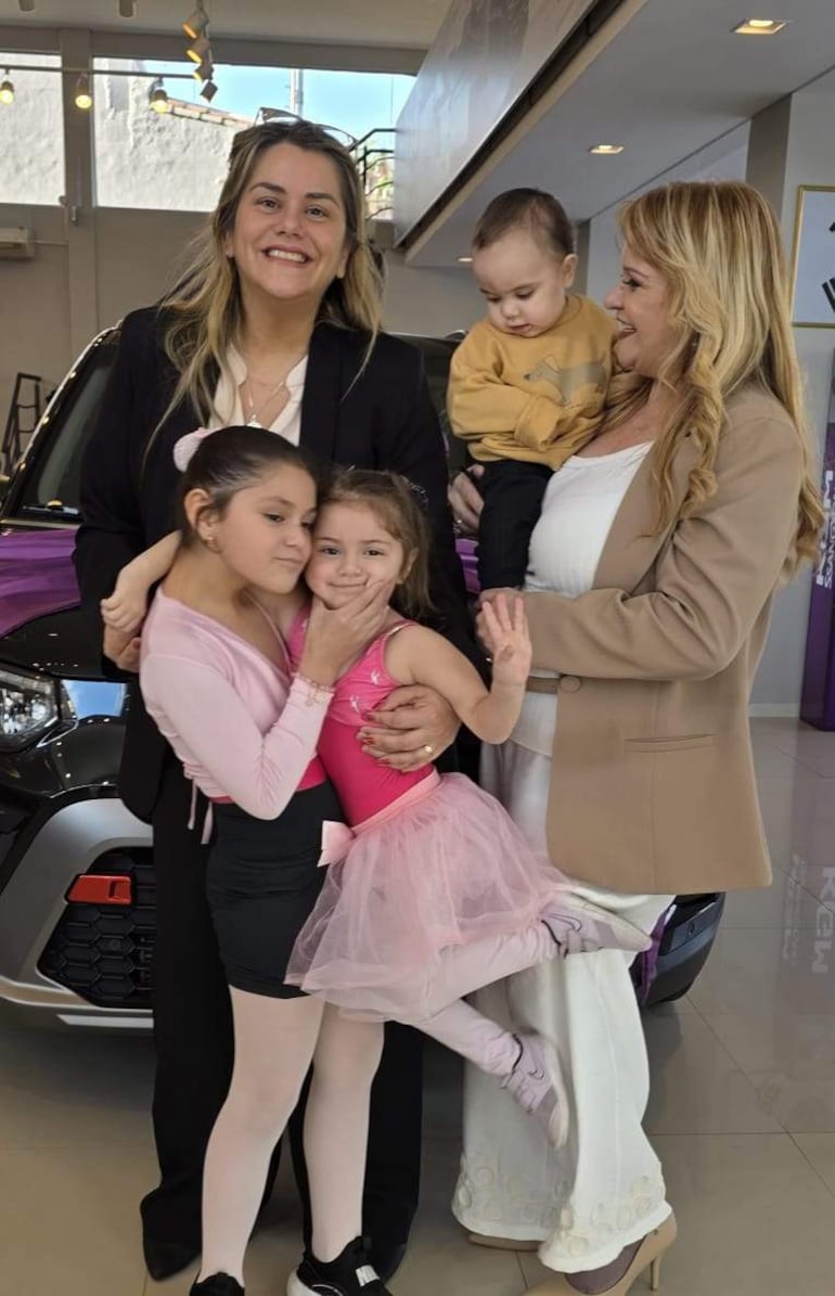 Tres niñas en vestuarios rosados abrazadas, con dos mujeres adultas tras ellas en un ambiente bien iluminado y moderno.