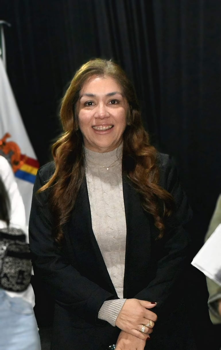 Fabiola Castelnovo sonríe con suéter claro y saco negro en un auditorio lleno de sombras de asistentes.