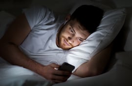 Hombre revisa el celular en la cama.