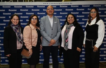 Cinco adultos bien vestidos sonríen en un evento, destacando a un hombre en chaleco gris y mujeres con bufandas coloridas.