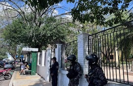 Mujer sentada en vestido blanco y grupo de personas en una parada de autobús, mientras agentes de seguridad observan atentos.