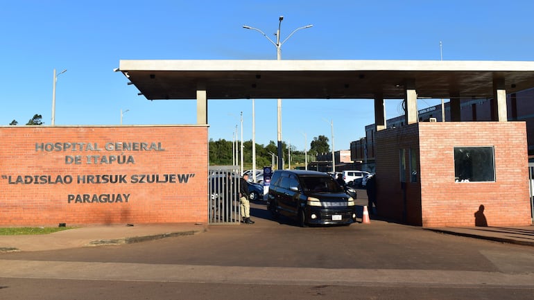 Guardia de seguridad junto a la reja del Hospital General de Itapúa, controlando un vehículo negro en un entorno ordenado.