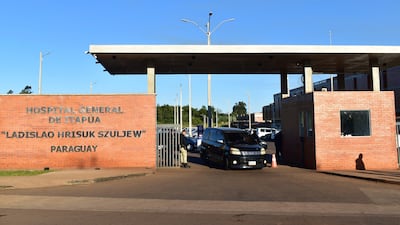 Guardia de seguridad junto a la reja del Hospital General de Itapúa, controlando un vehículo negro en un entorno ordenado.