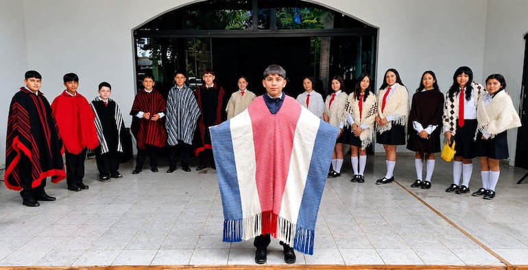 Adolescente con poncho rojo, azul y blanco, rodeado de jóvenes en ponchos tradicionales, en un ambiente de actividad cultural.