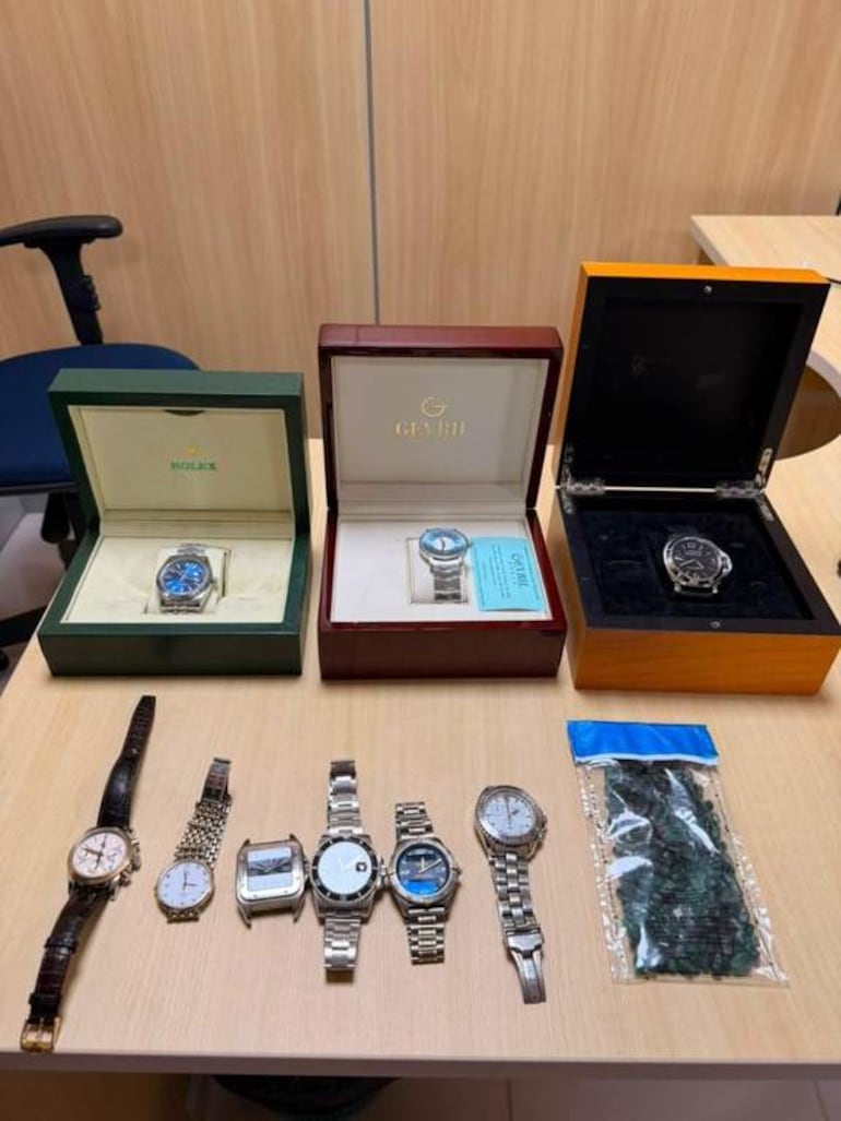 Varios relojes de lujo y estuches sobre una mesa de madera en un interior decorado.