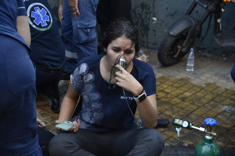 Mujer con máscara de oxígeno y expresión de malestar rodeada de rescatistas y botellas de agua en el suelo.