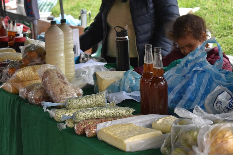 Mujer con abrigo oscuro atiende un puesto con productos alimenticios, mientras una niña organiza los artículos.