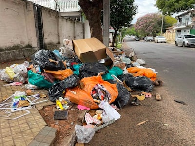 Acumulación de basura en la vereda, con bolsas y cartones en un entorno urbano desordenado.