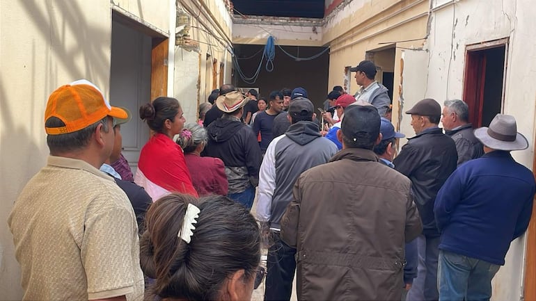 Hombre con gorra oscura habla a un grupo de personas en un ambiente informal, con paredes descascaradas y cables expuestos.