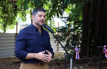 Oscar Andrés Rodríguez Quiñonez en camisa azul oscuro gesticulando frente a un micrófono, rodeado de vegetación.