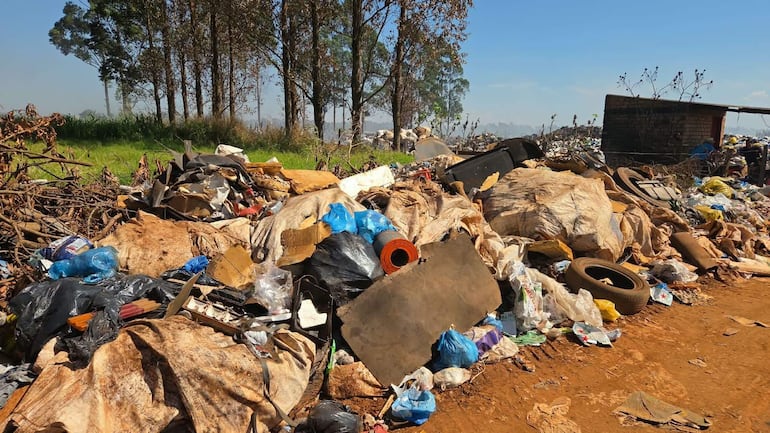 Acumulación de basura en Campo 9, entre neumáticos y plásticos, bajo un cielo despejado y árboles de fondo.