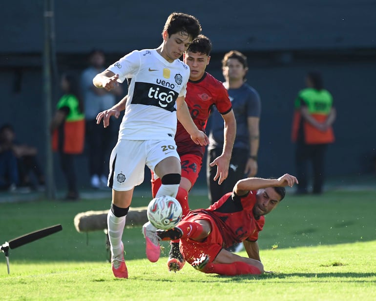 Jugador con camiseta blanca y número 20 evadiendo a un rival vestido de rojo y número 24 en un campo de fútbol.