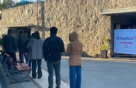 Grupo de seis personas de espaldas, con ropa abrigada, esperan ingresar a la feria de empleo en un entorno frío y formal.