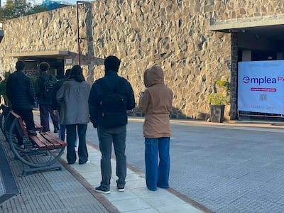 Grupo de seis personas de espaldas, con ropa abrigada, esperan ingresar a la feria de empleo en un entorno frío y formal.
