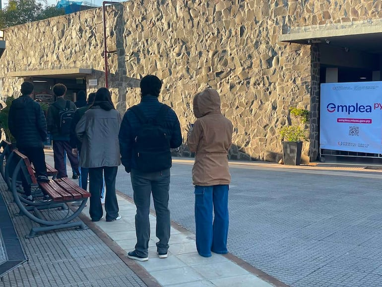 Grupo de seis personas de espaldas, con ropa abrigada, esperan ingresar a la feria de empleo en un entorno frío y formal.