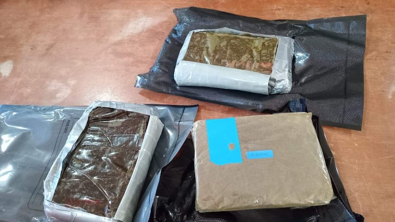 Tres paquetes de marihuana sobre mesa de madera, uno con etiqueta azul que dice 'BUSH-MINT'.