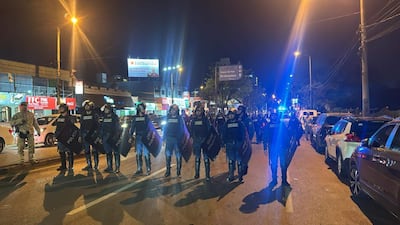 Seis policías en uniforme alineados, equipados con escudos, en una calle urbana iluminada de Encarnación.