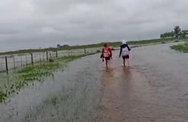 Dos alumnas caminan descalzas por el agua rumbo a la escuela de Tacuara’í.