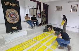 Esposados Fidel Lusichi (remera clara) y Camilo García (remera oscura) mientras los agentes ubican en el suelo la droga incautada.