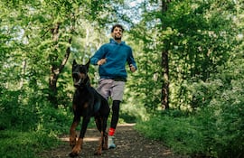 Hombre trota con su perro en un bosque.