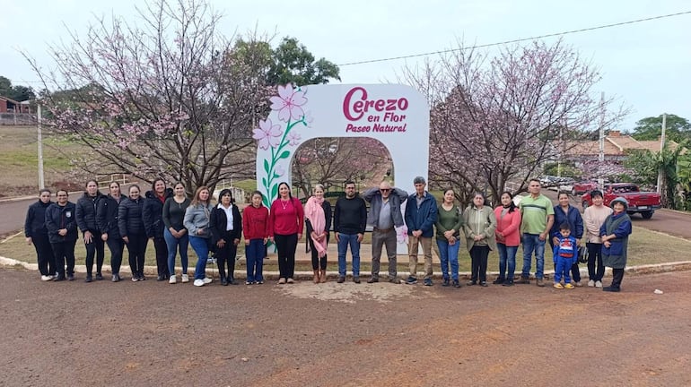 Grupo de personas, abrigadas, sonríen frente a un arco decorado con flores que dice 'Cerezo en Flor Paseo Natural'.