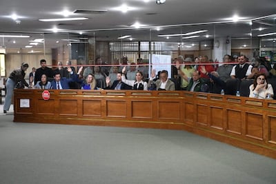 Felix Ayala y Paulina Serrano levantan las manos en votación en un ambiente formal, con muebles de madera.