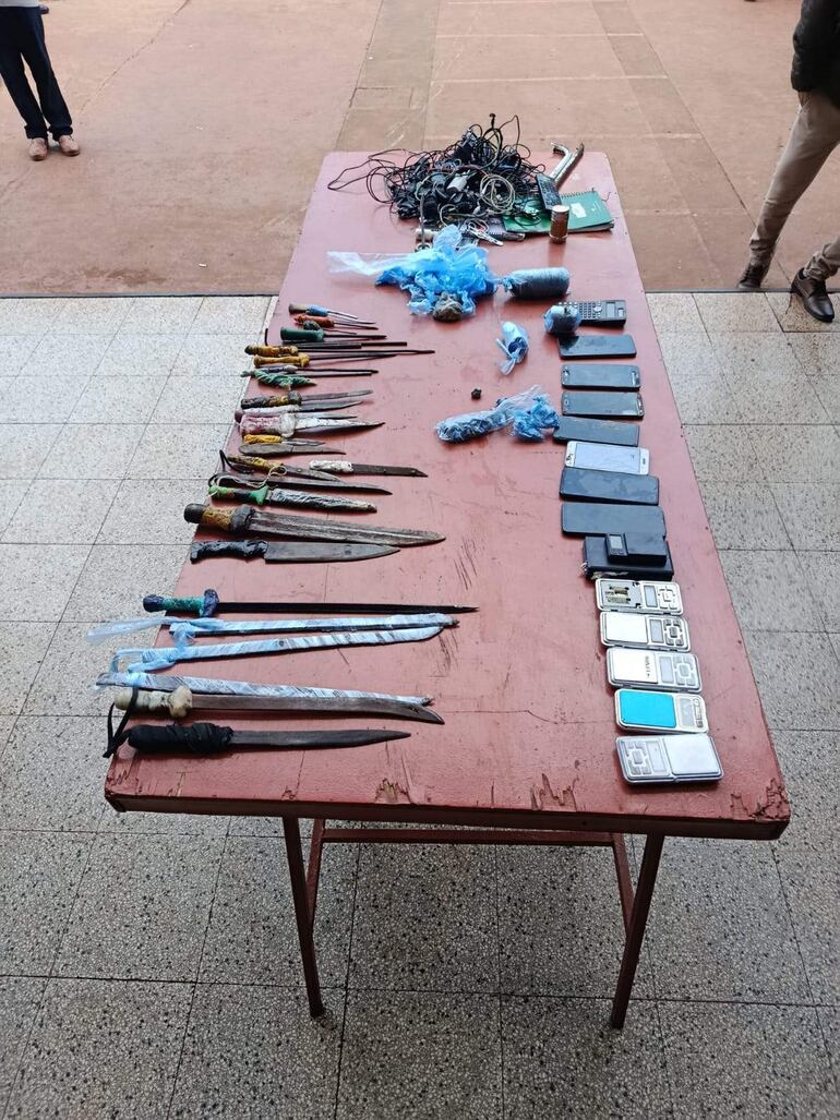 Mesa de madera con cuchillos, armas y teléfonos móviles confiscados en el patio del CERESO.