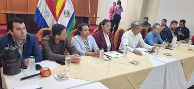 Reunión formal con Arsenio Zárate y diez personas sentadas, todos vestidos formalmente, conversando en ambiente sobrio y bien iluminado.
