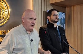 Kobylanski en camisa clara frente a un fondo con el escudo de Paraguay, mientras otro hombre con abrigo negro lo escucha.