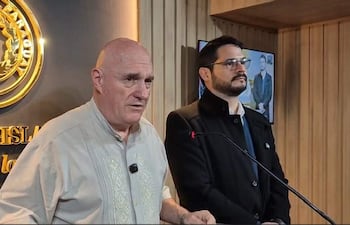 Kobylanski en camisa clara frente a un fondo con el escudo de Paraguay, mientras otro hombre con abrigo negro lo escucha.