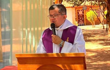 El presbítero Cristino Ramos González, vestido de blanco con estola morada, sostiene un micrófono y se muestra concentrado ante un auditorio desconocido.