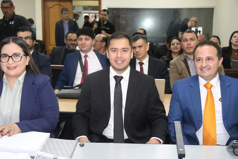Miguel Prieto en traje negro sonríe entre sus defensores en un ambiente formal de tribunal.