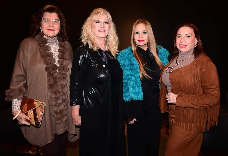Cuatro mujeres posan ante la cámara, vistiendo abrigos de diferentes colores y estilos en ambiente interior oscuro.