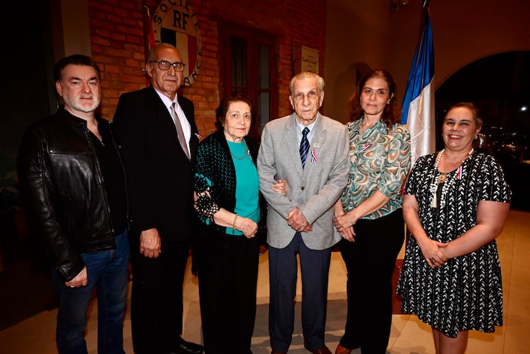 Seis personas, dos hombres en trajes y cuatro mujeres elegantes, junto a una bandera en el Club Centenario.