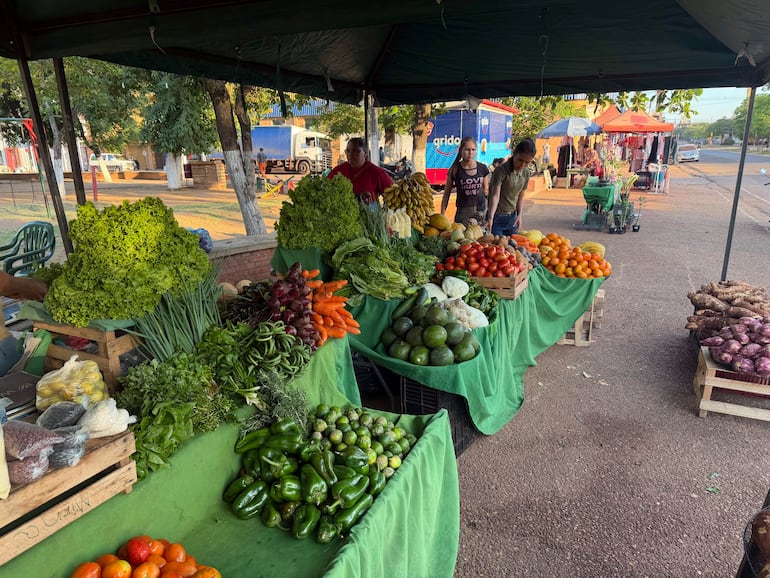 Dos hombres detrás de una mesa con verduras, y una pareja seleccionando frutas en un mercado al aire libre con manteles verdes.