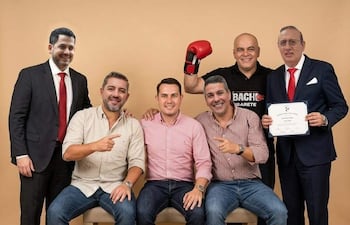 Rivas sonríe sosteniendo un certificado con guantes de boxeo, rodeado de amigos que lo apoyan con sonrisas.